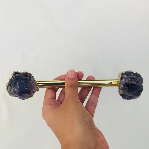 Gold cabinet handle with rough amethyst agate knob ends held by a hand