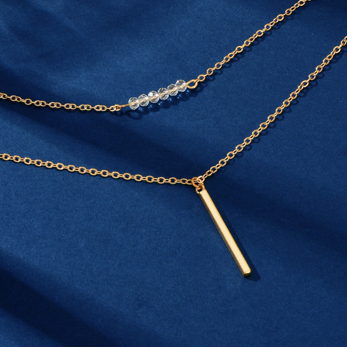 Gold-tone necklace close-up: layered chains with vertical bar charm and bead details