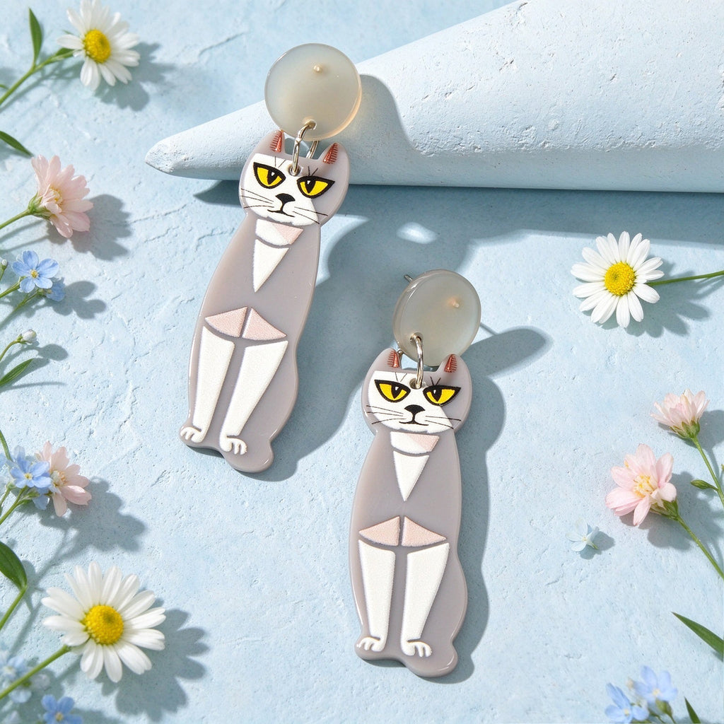 Two grey acrylic cat dangle earrings with gold hooks, cartoon faces, and geometric bodies