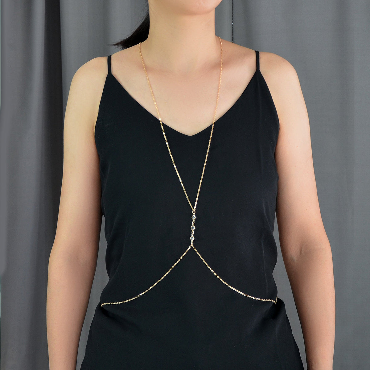 Gold-tone body chain harness draped over black V-neck camisole with charm centerpiece