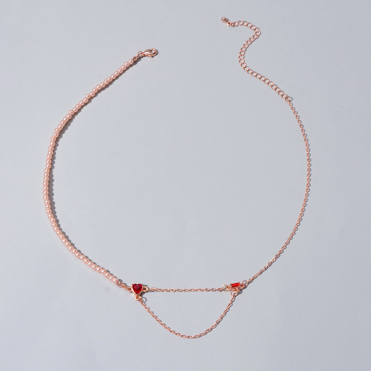 Rose gold tone chain necklace with red crystal heart drop motif, flat lay