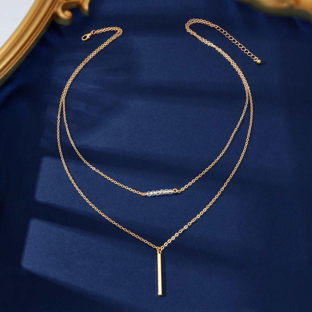 Gold-tone layered chain necklace with dangling vertical bar charm and fine link detail