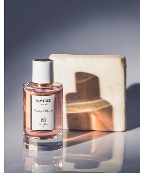 Perfume bottle with white cap and pink glass beside cardboard gift box.