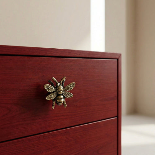 Antique brass bee drawer knob on dark wooden cabinet drawer front