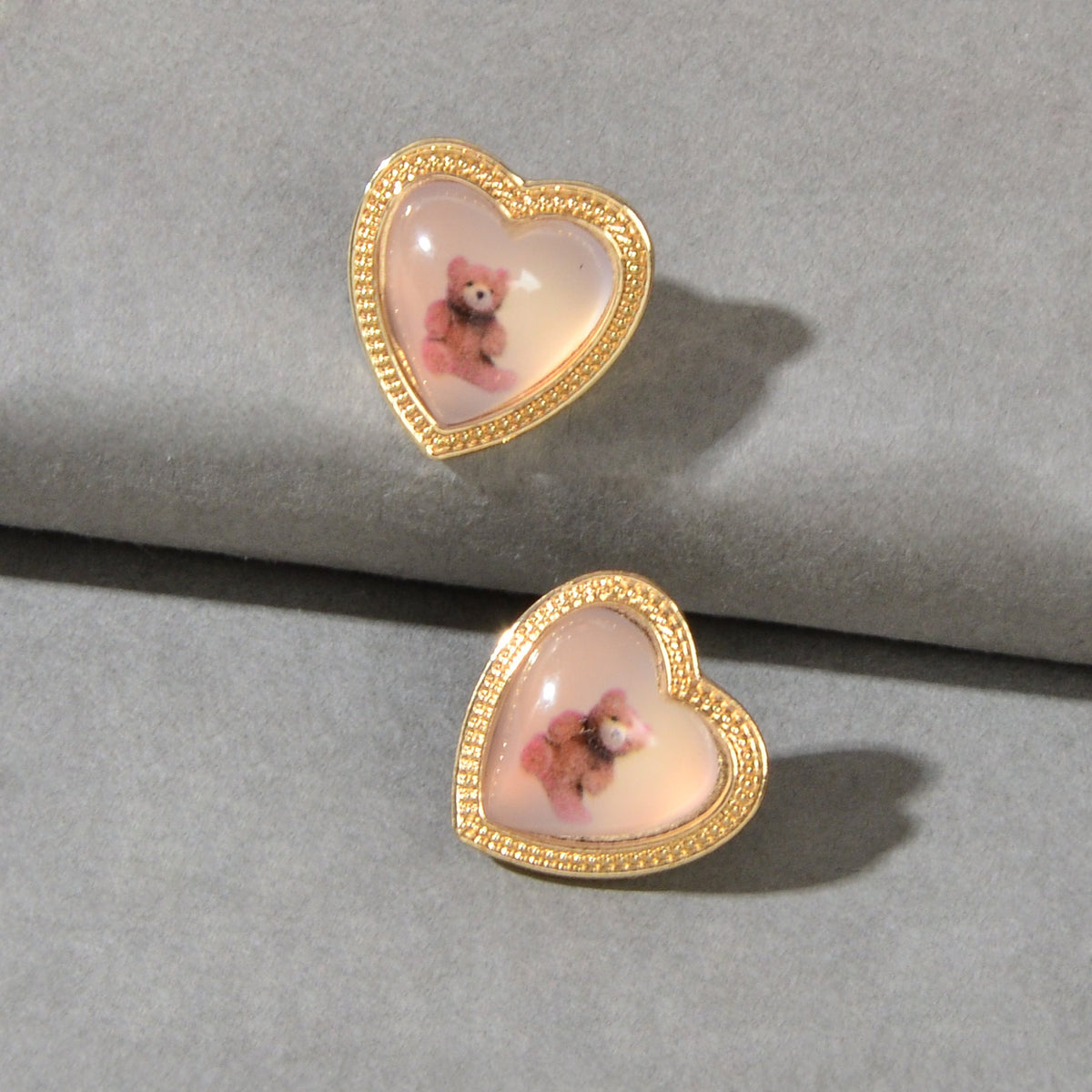 Two gold heart resin stud earrings with pink bear images, angled view