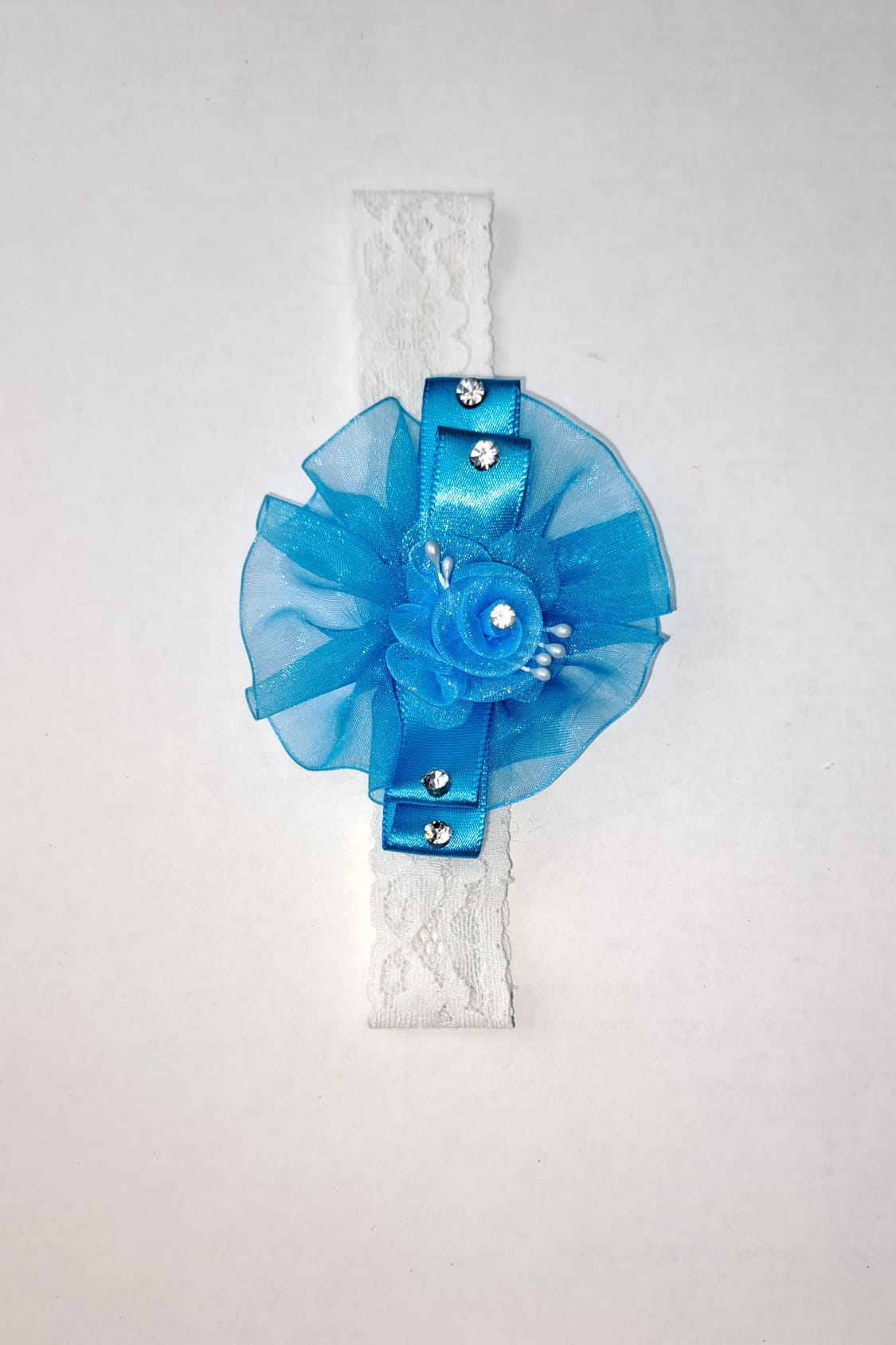 Blue ruffle flower baby headband with organza bow and rhinestone accents on white lace