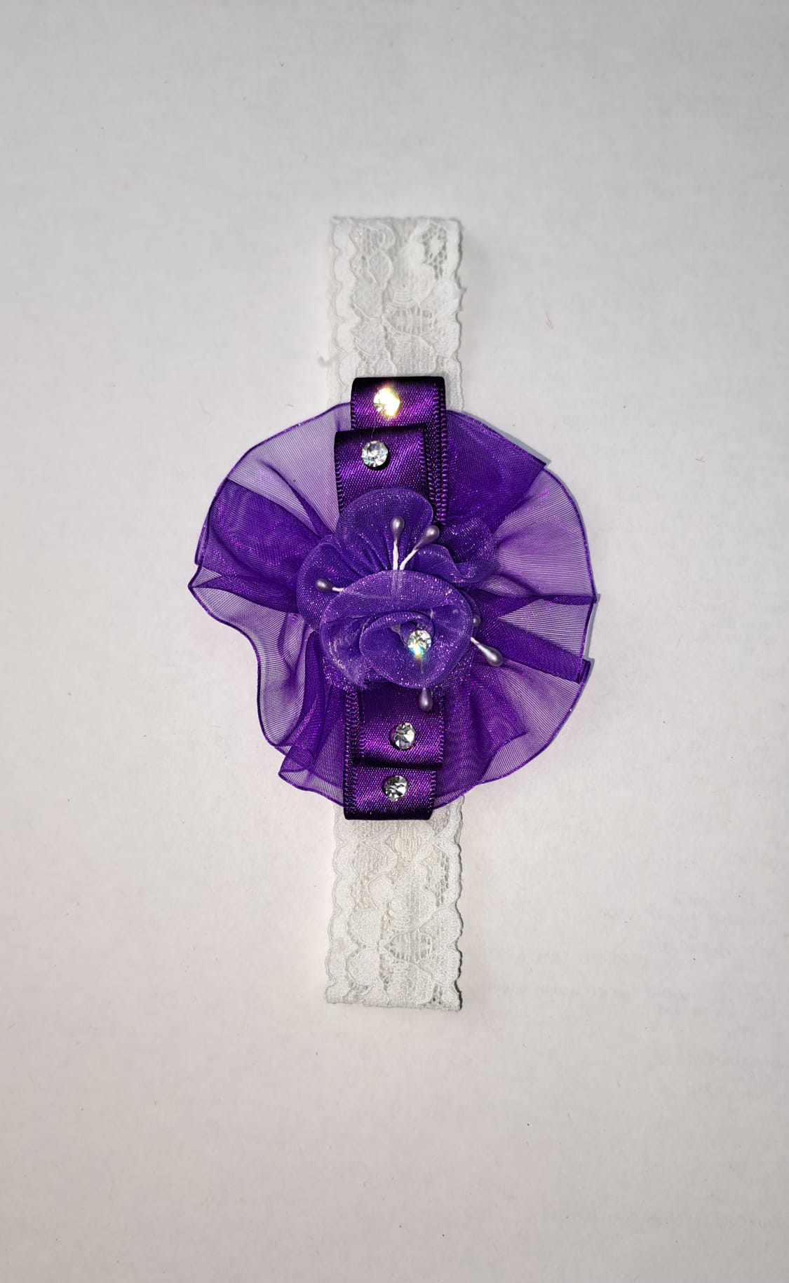 Purple ruffle flower baby headband with organza bow and rhinestone accents on white lace
