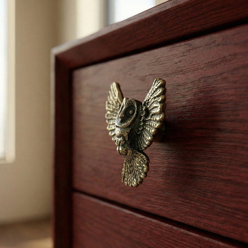 Antique brass owl drawer knob with raised wings, mounted on drawer front