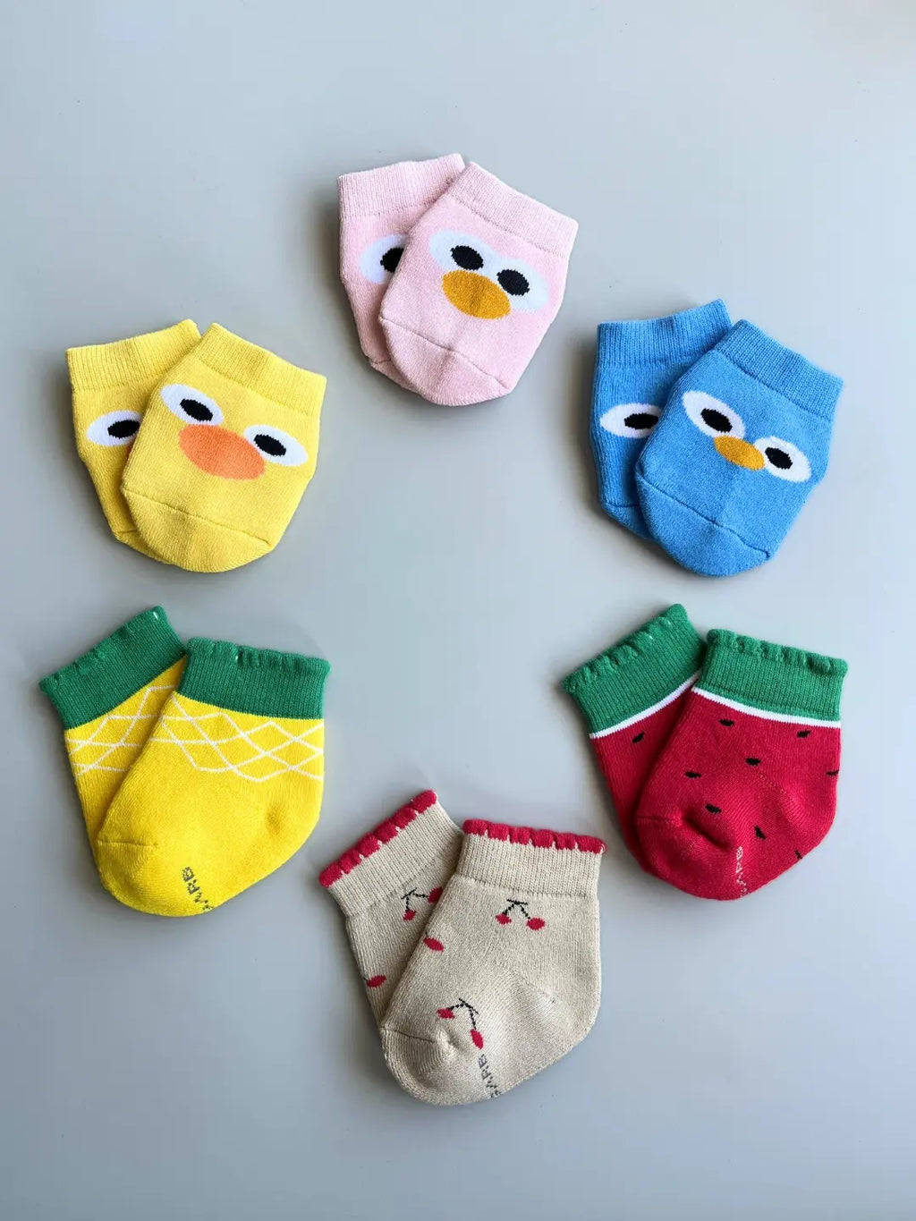Air Garb brand baby combo socks for infants; a 6-pair set of soft cotton socks featuring pineapple, watermelon, cherry, and cute character face designs in vibrant colors like yellow, red, and blue.