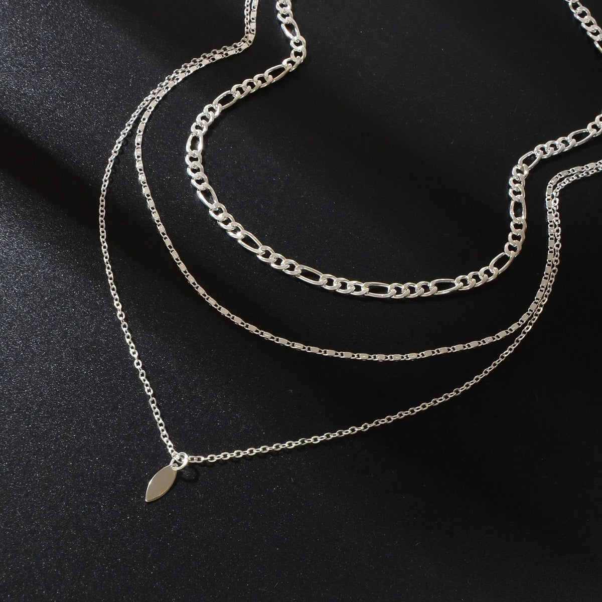 Close-up layered silver-tone choker necklace with small leaf drop charm on chain